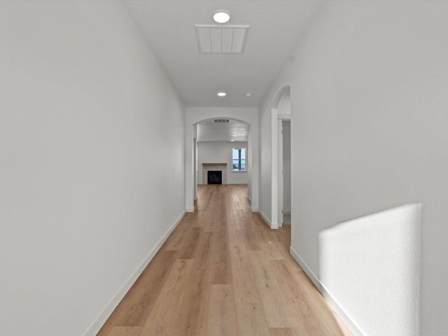 hallway featuring baseboards, visible vents, arched walkways, and light wood-style flooring