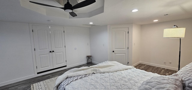 bedroom with a raised ceiling, ceiling fan, dark hardwood / wood-style floors, and a closet