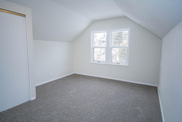 bonus room with a textured ceiling, lofted ceiling, and dark carpet