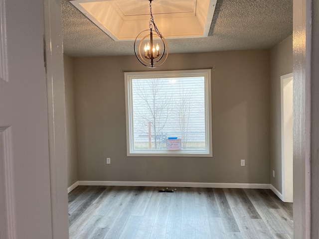 spare room with a textured ceiling, hardwood / wood-style flooring, and a notable chandelier