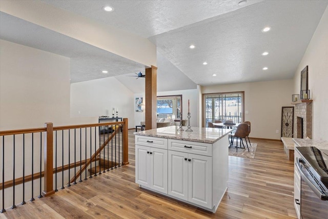 kitchen with white cabinetry, stainless steel electric range, lofted ceiling, light wood-type flooring, and light stone countertops