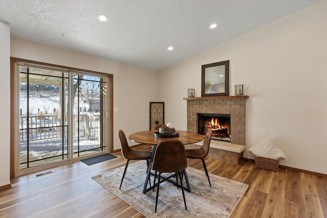 dining space with a fireplace, light hardwood / wood-style flooring, a textured ceiling, and lofted ceiling