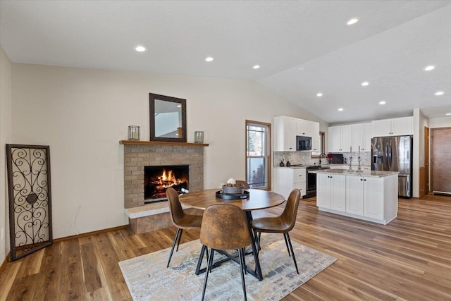 dining room with a brick fireplace, light wood-type flooring, and vaulted ceiling