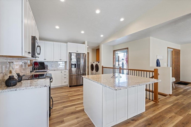 kitchen featuring stainless steel appliances, light stone countertops, white cabinets, washing machine and dryer, and a kitchen island