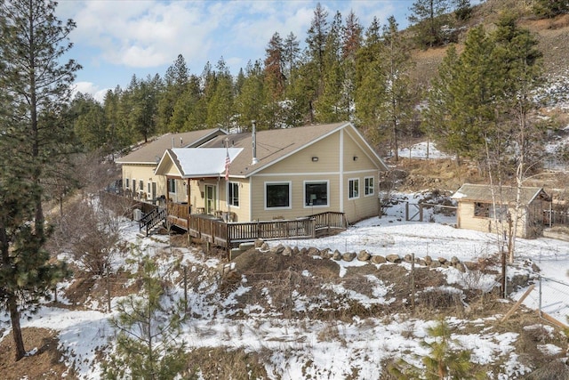 snow covered rear of property featuring a deck and a storage unit