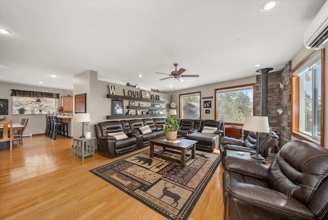 living room with a wall unit AC, ceiling fan, a wood stove, and light hardwood / wood-style floors