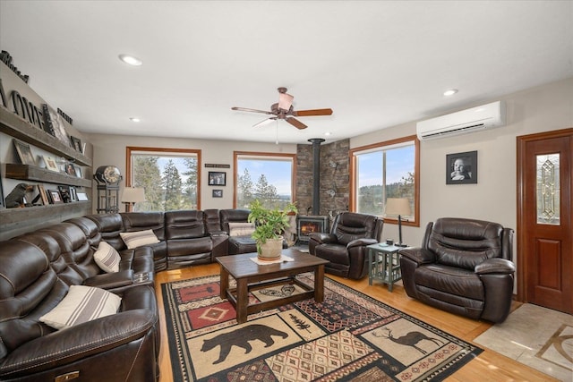 living room with a wall mounted air conditioner, light hardwood / wood-style floors, a wood stove, and ceiling fan