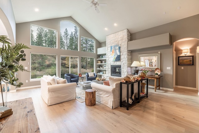 living room with ceiling fan, high vaulted ceiling, light hardwood / wood-style floors, and a stone fireplace