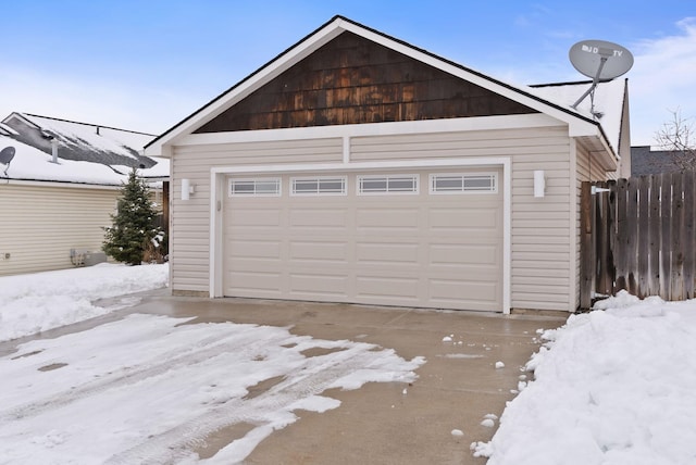 snow covered garage with a garage and fence