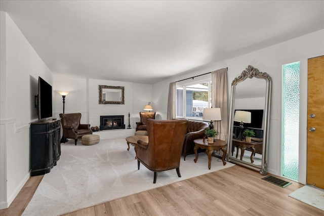 living room with a brick fireplace, visible vents, and light wood-style flooring