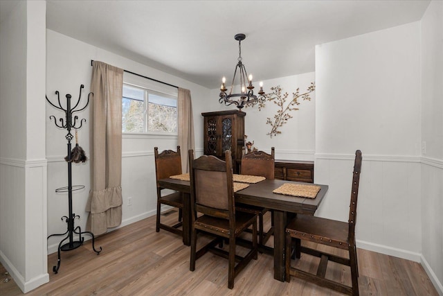 dining area with a chandelier, light wood finished floors, and wainscoting