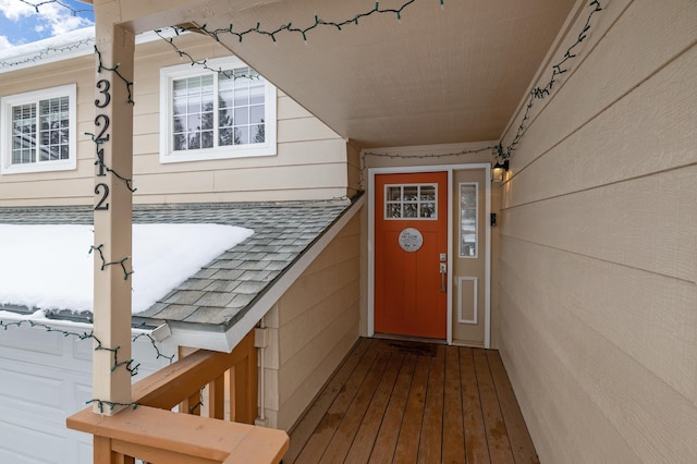 snow covered property entrance with a shingled roof