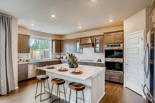 kitchen with stainless steel appliances, premium range hood, a kitchen island, light countertops, and brown cabinetry