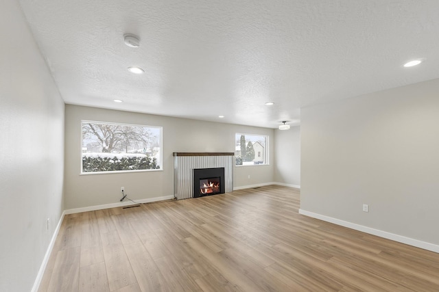 unfurnished living room with a glass covered fireplace, baseboards, a textured ceiling, and light wood finished floors