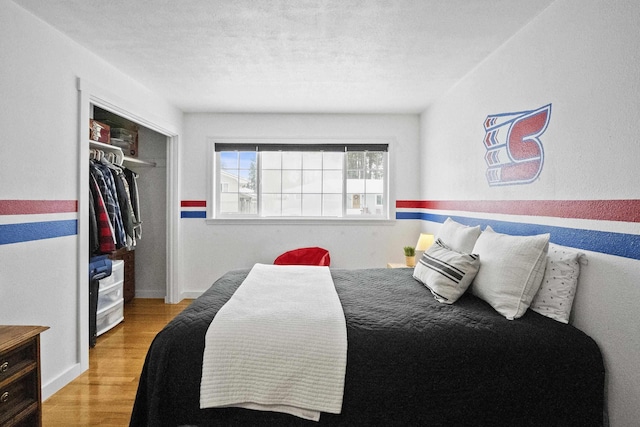 bedroom featuring a textured ceiling, a closet, light wood-type flooring, and baseboards