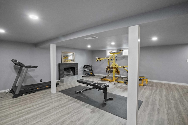 exercise room featuring light wood-style flooring, a fireplace, visible vents, and baseboards