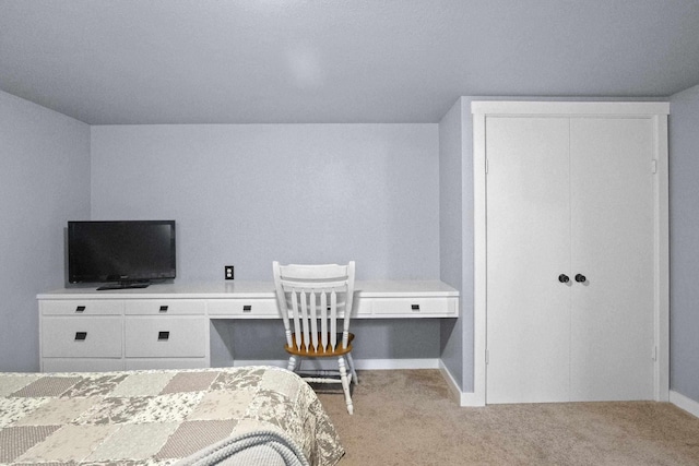 bedroom featuring a closet, built in study area, light carpet, and baseboards