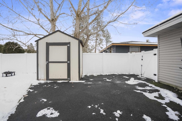 snow covered structure featuring an outbuilding, a shed, and a fenced backyard