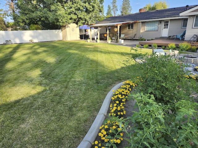 view of yard with a fenced backyard, a storage unit, a wooden deck, and an outbuilding