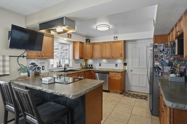 kitchen with a peninsula, appliances with stainless steel finishes, brown cabinetry, and dark countertops