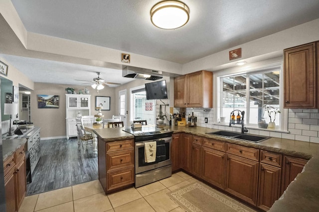 kitchen featuring dark countertops, brown cabinets, a peninsula, stainless steel range with electric stovetop, and a sink