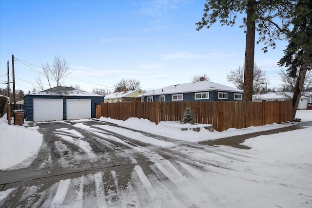 yard covered in snow with a garage, an outbuilding, and fence