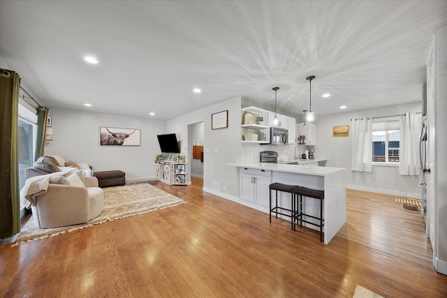 living area featuring a textured ceiling, recessed lighting, light wood-type flooring, and baseboards