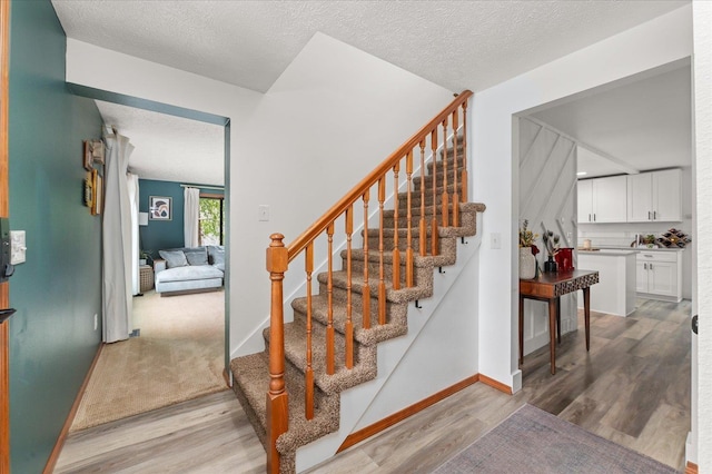 stairway with a textured ceiling, baseboards, and wood finished floors