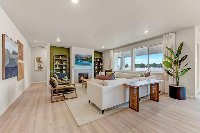 living area with a glass covered fireplace, visible vents, light wood finished floors, and recessed lighting