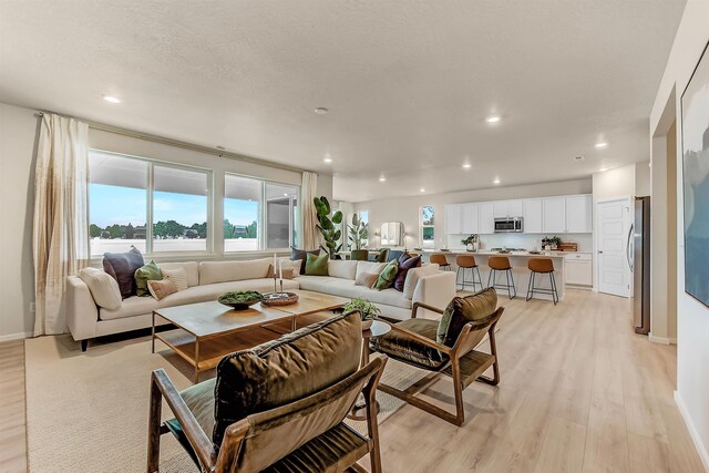 living room featuring a textured ceiling, light wood-type flooring, baseboards, and recessed lighting