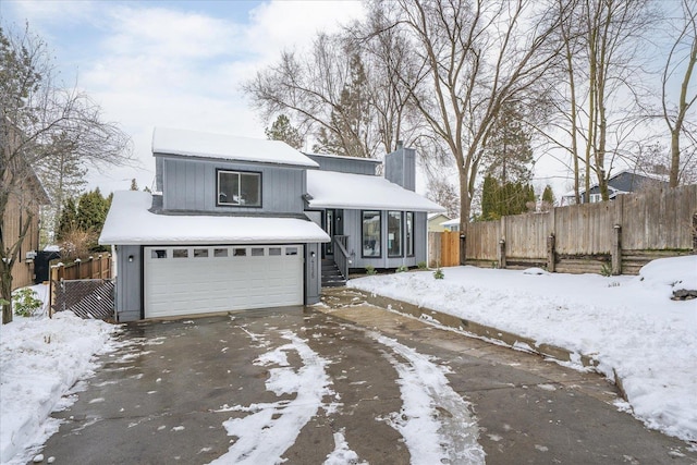 view of front of house featuring an attached garage, driveway, a chimney, and fence