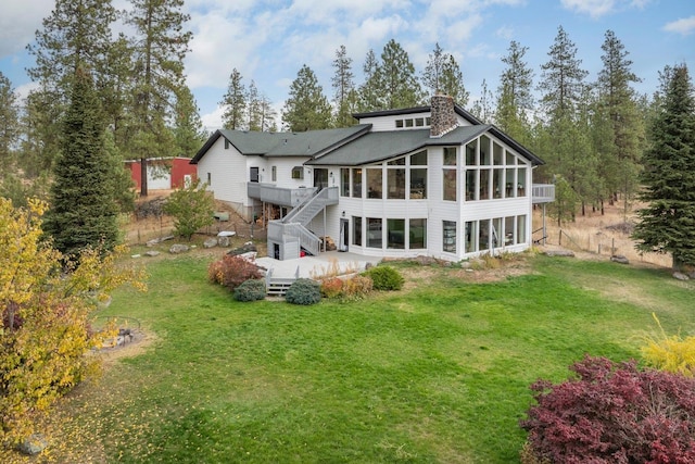 rear view of house featuring a sunroom, a yard, stairway, a wooden deck, and a chimney