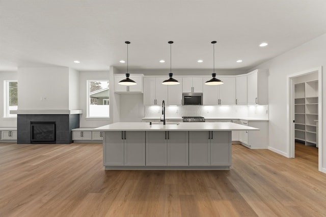 kitchen featuring light wood-style flooring, an island with sink, a sink, stainless steel microwave, and white cabinetry