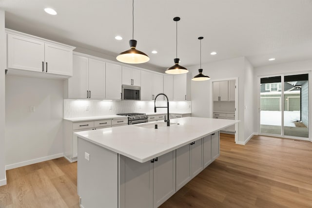 kitchen with a kitchen island with sink, a sink, white cabinetry, appliances with stainless steel finishes, and decorative backsplash