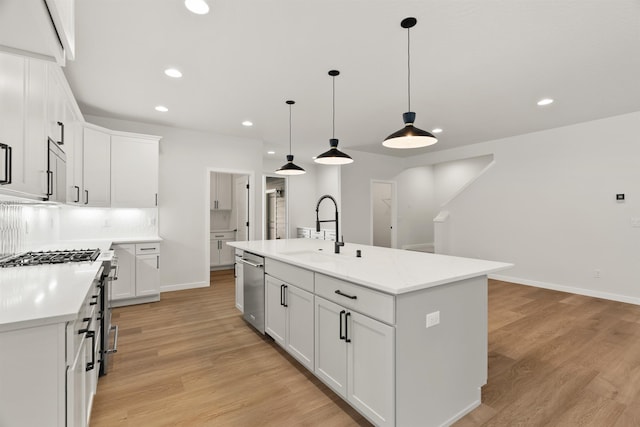 kitchen with light wood-style flooring, a center island with sink, a sink, recessed lighting, and light countertops