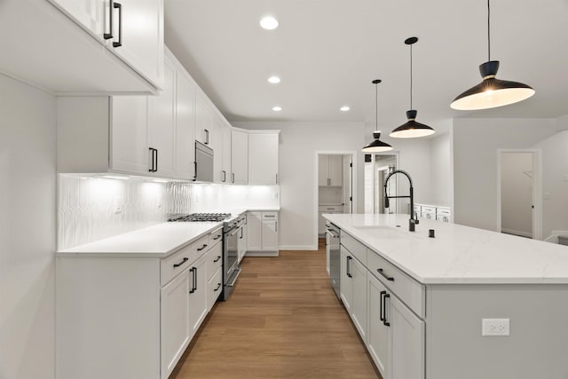 kitchen with backsplash, appliances with stainless steel finishes, light wood-style floors, white cabinetry, and a sink