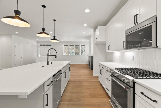 kitchen with a sink, light wood-style floors, appliances with stainless steel finishes, white cabinetry, and tasteful backsplash