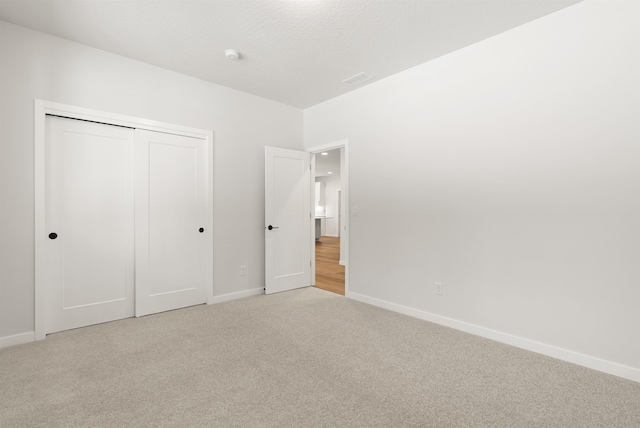 unfurnished bedroom featuring a closet, baseboards, light colored carpet, and a textured ceiling