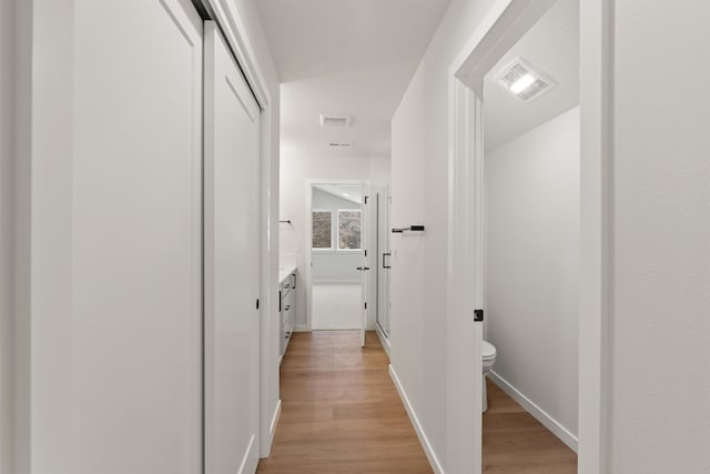 corridor with light wood-style floors, visible vents, and baseboards