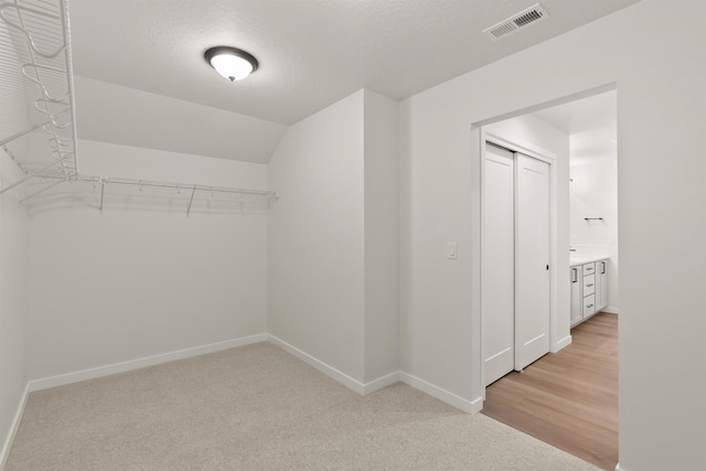 walk in closet with lofted ceiling, visible vents, and light carpet