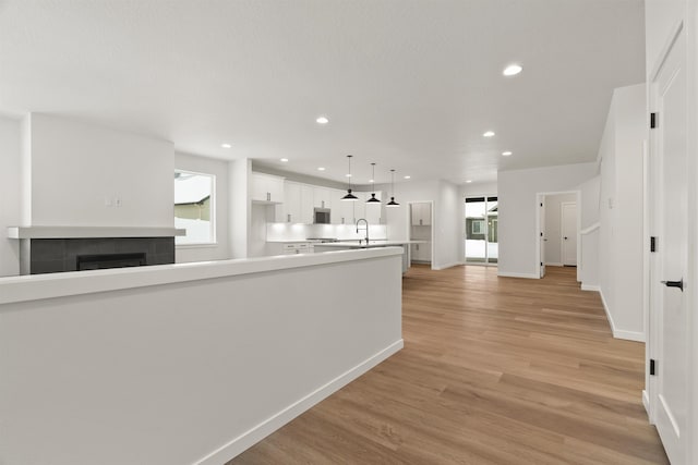corridor with recessed lighting, light wood-type flooring, baseboards, and a sink