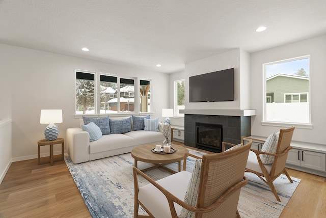 living room with recessed lighting, baseboards, a tiled fireplace, and light wood finished floors