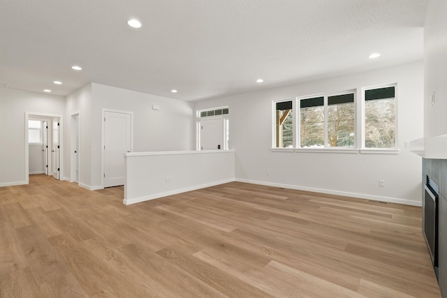 unfurnished living room with light wood-type flooring, plenty of natural light, and a tile fireplace