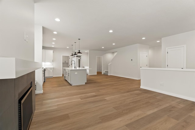 interior space featuring open floor plan, light wood-type flooring, light countertops, recessed lighting, and a kitchen island with sink