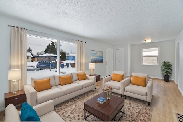 living room featuring light wood-style floors, visible vents, baseboards, and a textured ceiling