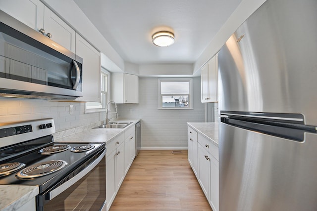 kitchen featuring white cabinets, light stone countertops, stainless steel appliances, light wood-type flooring, and a sink