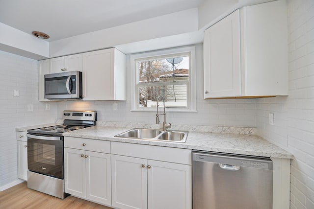 kitchen with white cabinets, light wood-style flooring, appliances with stainless steel finishes, a sink, and backsplash