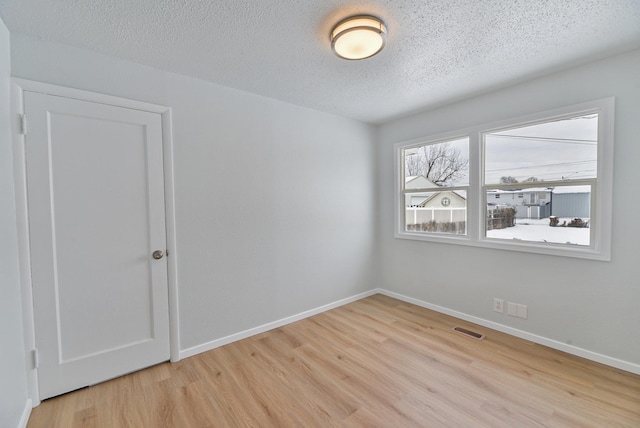 unfurnished room with a textured ceiling, light wood-type flooring, visible vents, and baseboards