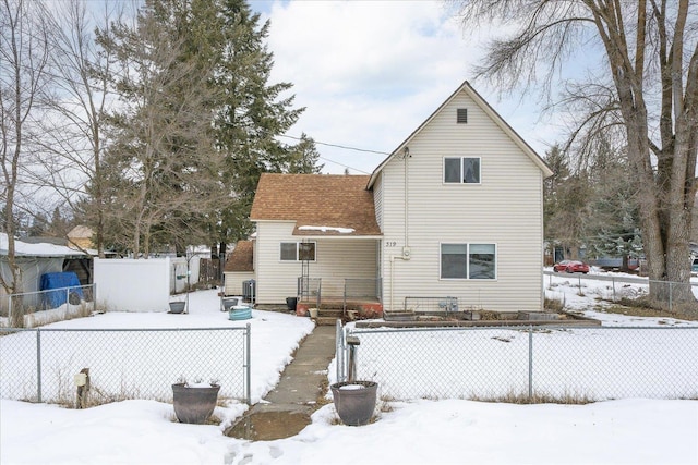 snow covered rear of property with a shingled roof and fence