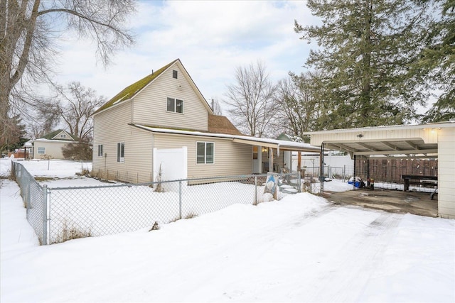 snow covered back of property with a carport, a porch, and fence